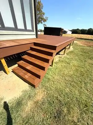 Brown deck with stairs attached to gray house in rural Kentucky under a blue sky