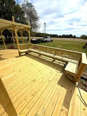 New wooden deck with built-in seating and pergola frame on rural Kentucky property