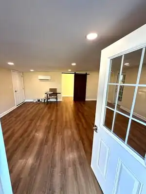 Interior room with wood-look laminate floor, beige walls, white trim, sliding barn door, and glass-paneled door