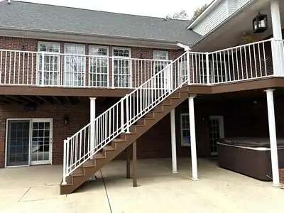 Brick home with brown deck and white railing stairs, outdoor patio and hot tub