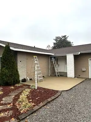 Exterior of a house with a new concrete front porch, two ladders, white stone columns, tan siding, landscaped bed.