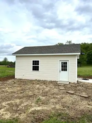 Beige vinyl-sided shed with white door and window in a rural Kentucky setting