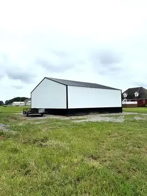 White metal storage building with black base trim on a gravel pad in rural Murray KY